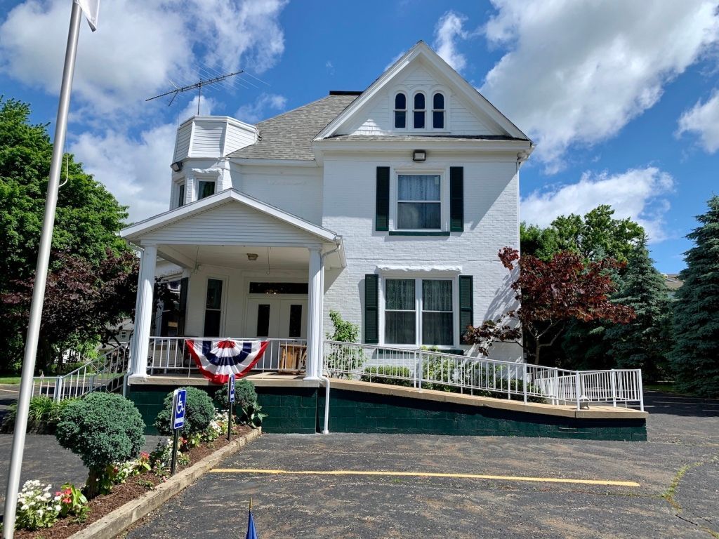 White historic house with porch, black shutters, and red-white-blue bunting under a blue sky