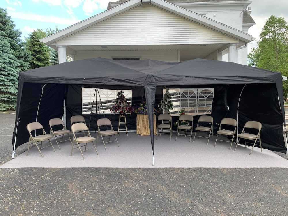 Black canopy tent with folding chairs set up on a driveway in front of a garage