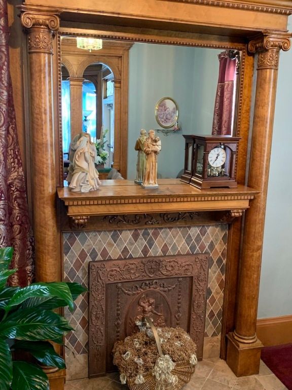 Ornate fireplace mantel with statues, mirror, clock, and floral arrangement in a decorated room