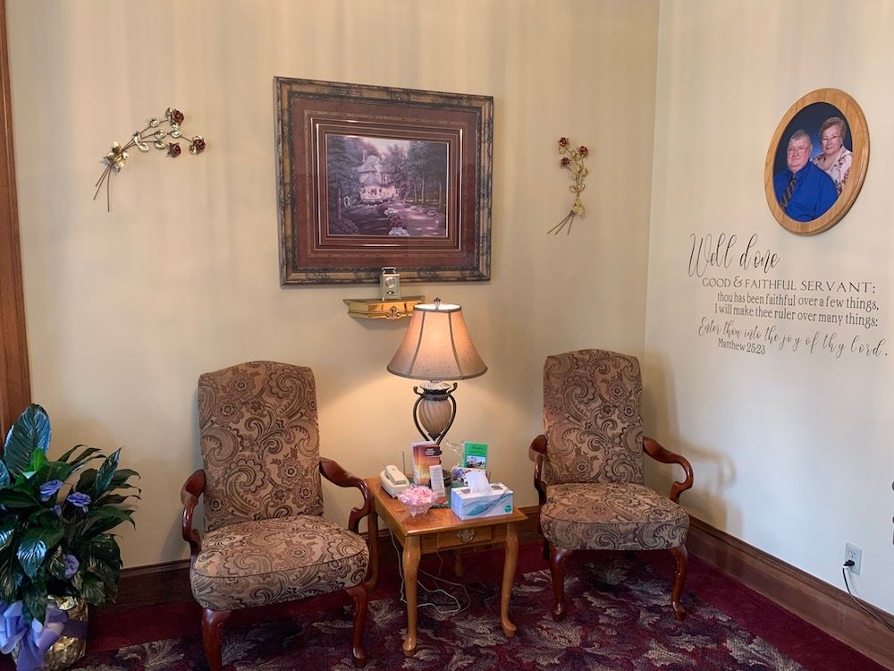 Cozy waiting room corner with two patterned armchairs, a lamp table, wall art, and floral decor