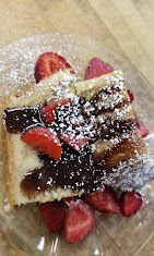 Strawberry-topped dessert on a plate, dusted with powdered sugar.