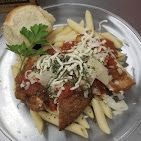 Plated pasta with tomato sauce, breaded cutlet, grated cheese, and a lemon wedge, with bread on the side