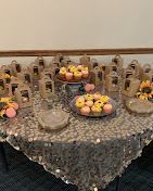 Dessert table with lace cloth, glass jars, fruit bowl, and small pastries arranged in a banquet hall