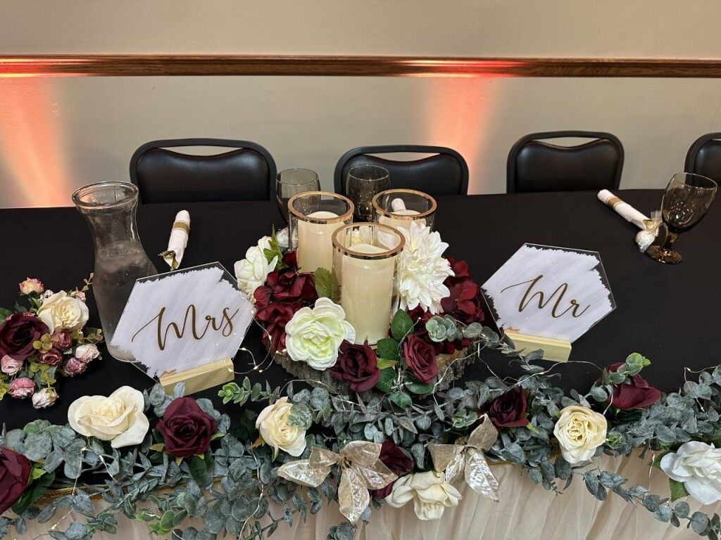 Elegant banquet table centerpiece with white and burgundy flowers, candles, and “Mr” and “Mrs” signs