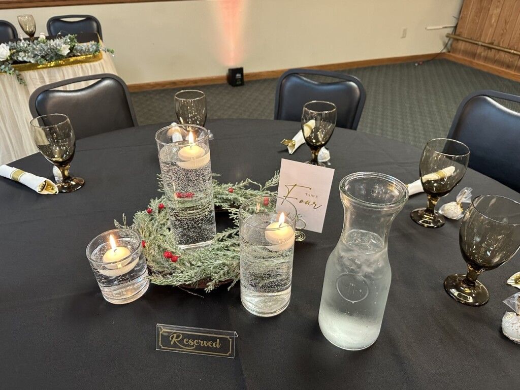 Decorated banquet table with black linens, gold goblets, candles, and frosted glass centerpieces