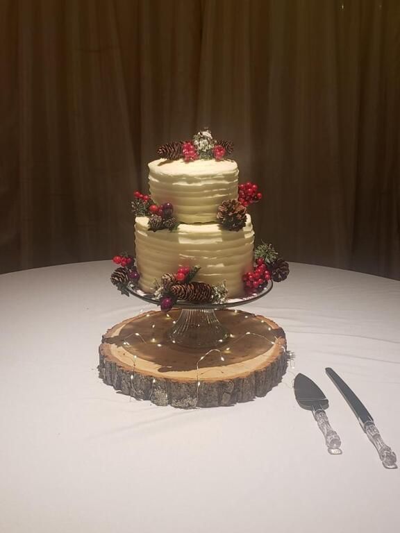 Tiered cream cake with red berries on a round chocolate base, displayed on a table with serving utensils