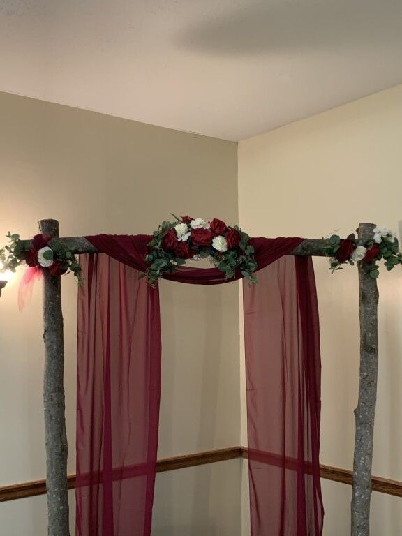 Red floral arch with burgundy drapes in a corner room, decorated for an event