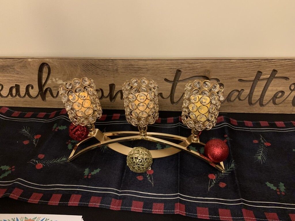 Decorative gold candle holders and red ornaments on a wooden shelf above a patterned runner