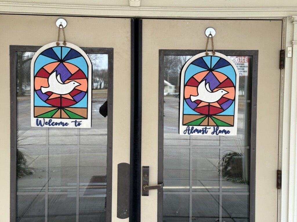 Two glass doors with colorful circular dove stained-glass signs hanging above the handles.