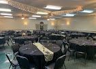 Empty banquet hall with round tables, black chairs, and ceiling lights