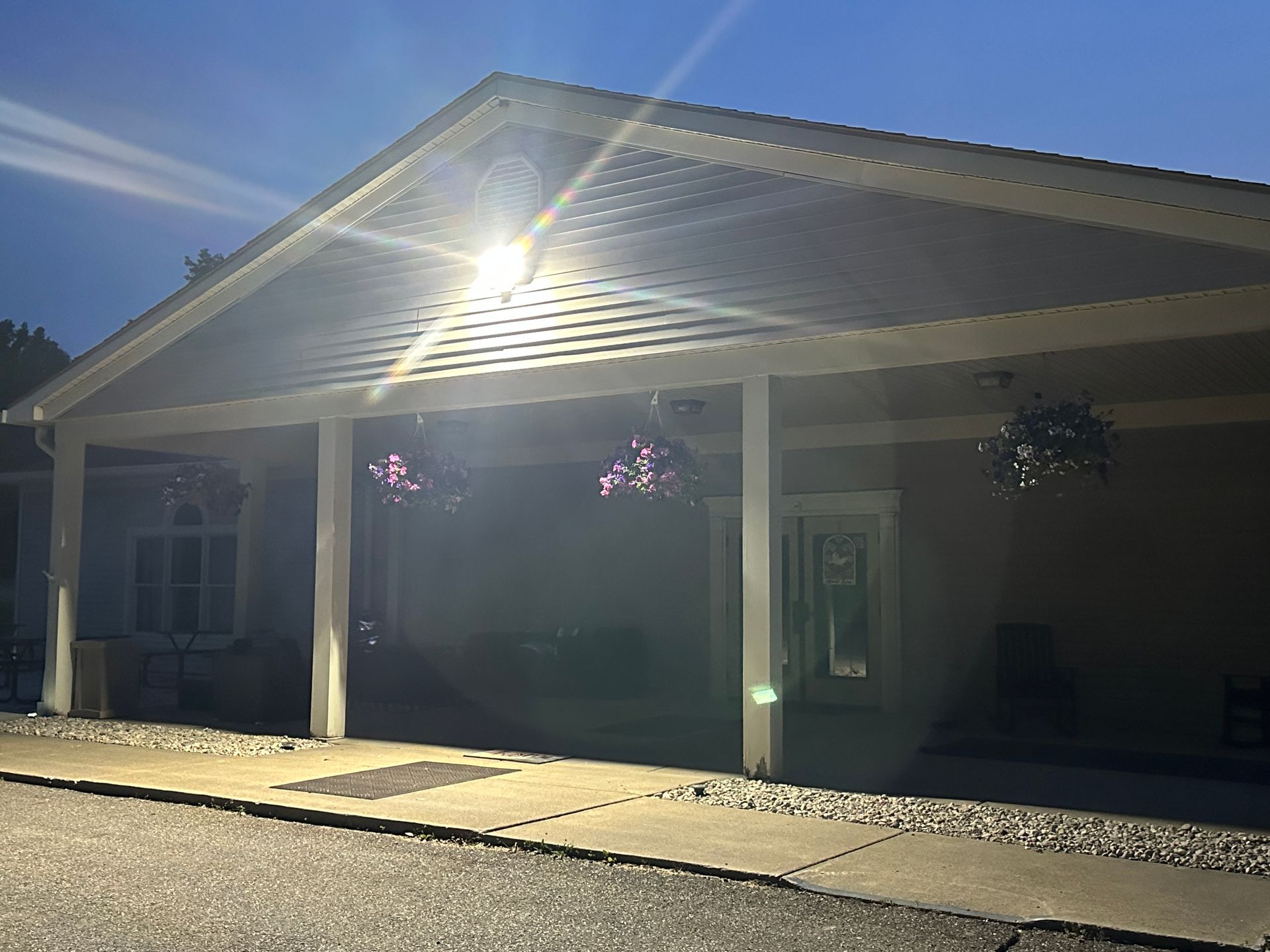 Sunlit covered front porch with white columns and hanging plants on a house under a clear blue sky
