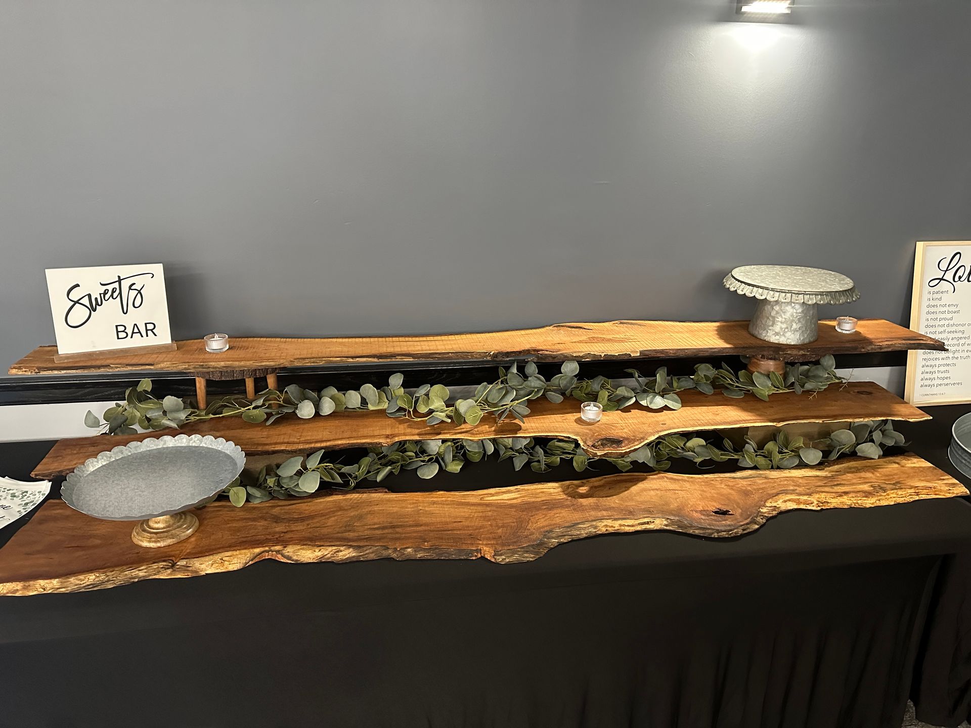 Buffet display of assorted food on wooden trays with small signs and silver serving bowls