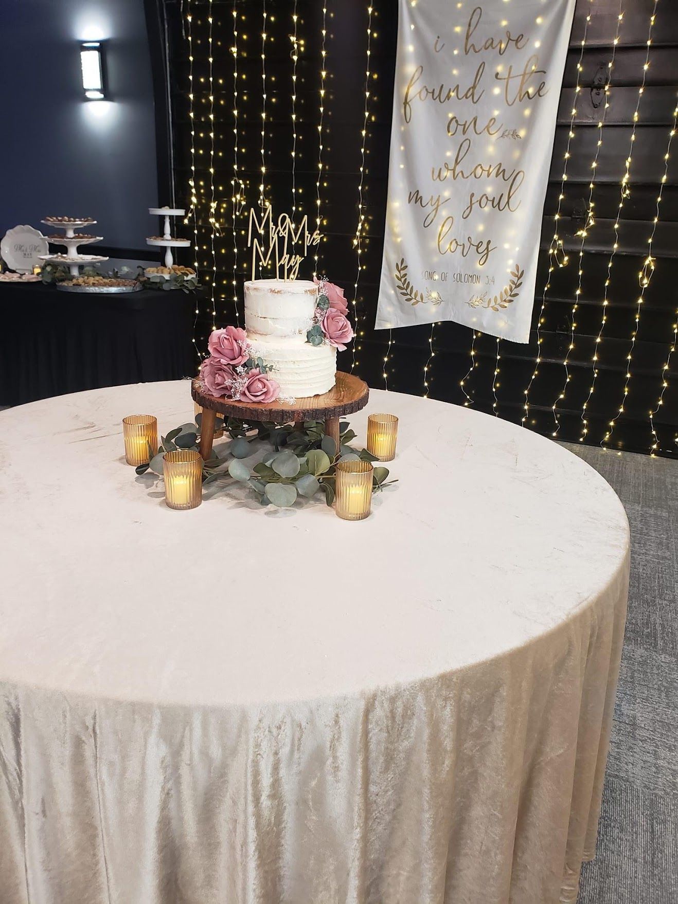 Decorated round table with a white cake, flowers, candles, and twinkling lights in a party venue