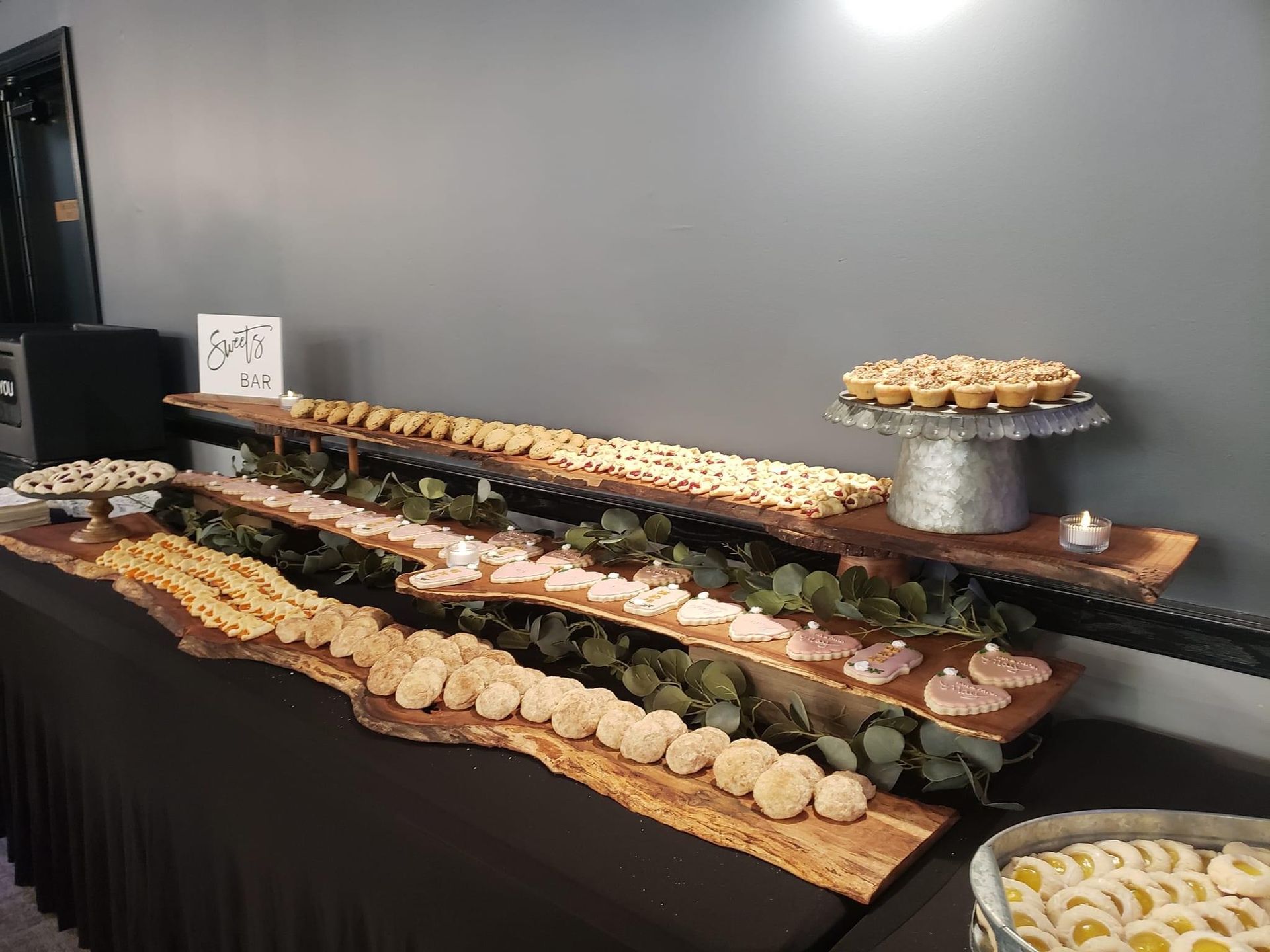 Long buffet table with assorted pastries and sweets on trays in a gray room