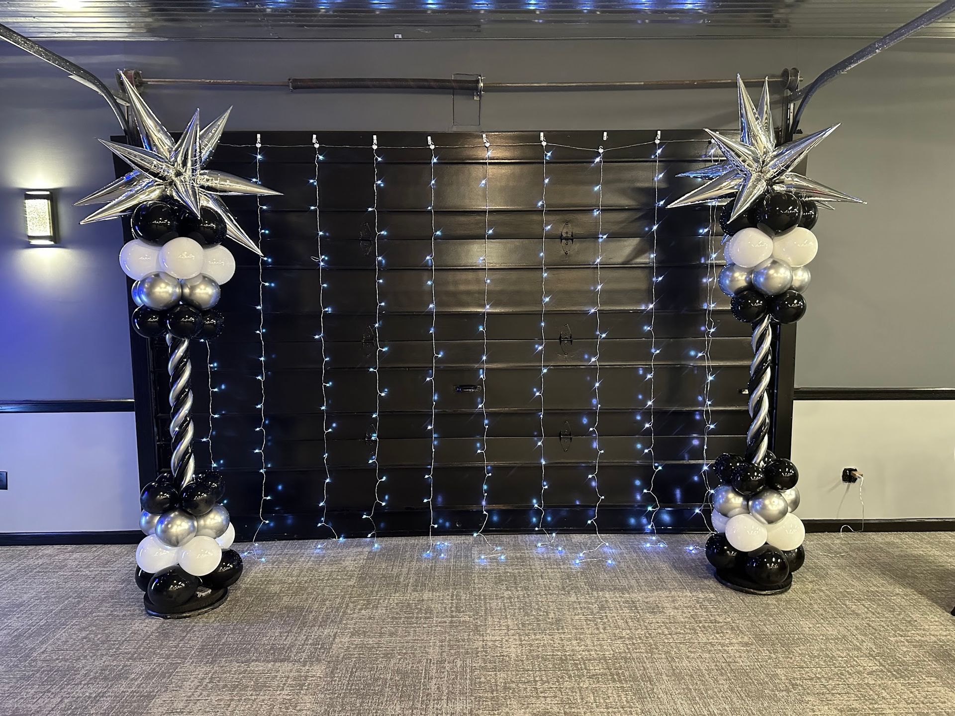 Decorated black and silver balloon arch framing a dark curtain backdrop in an indoor event space