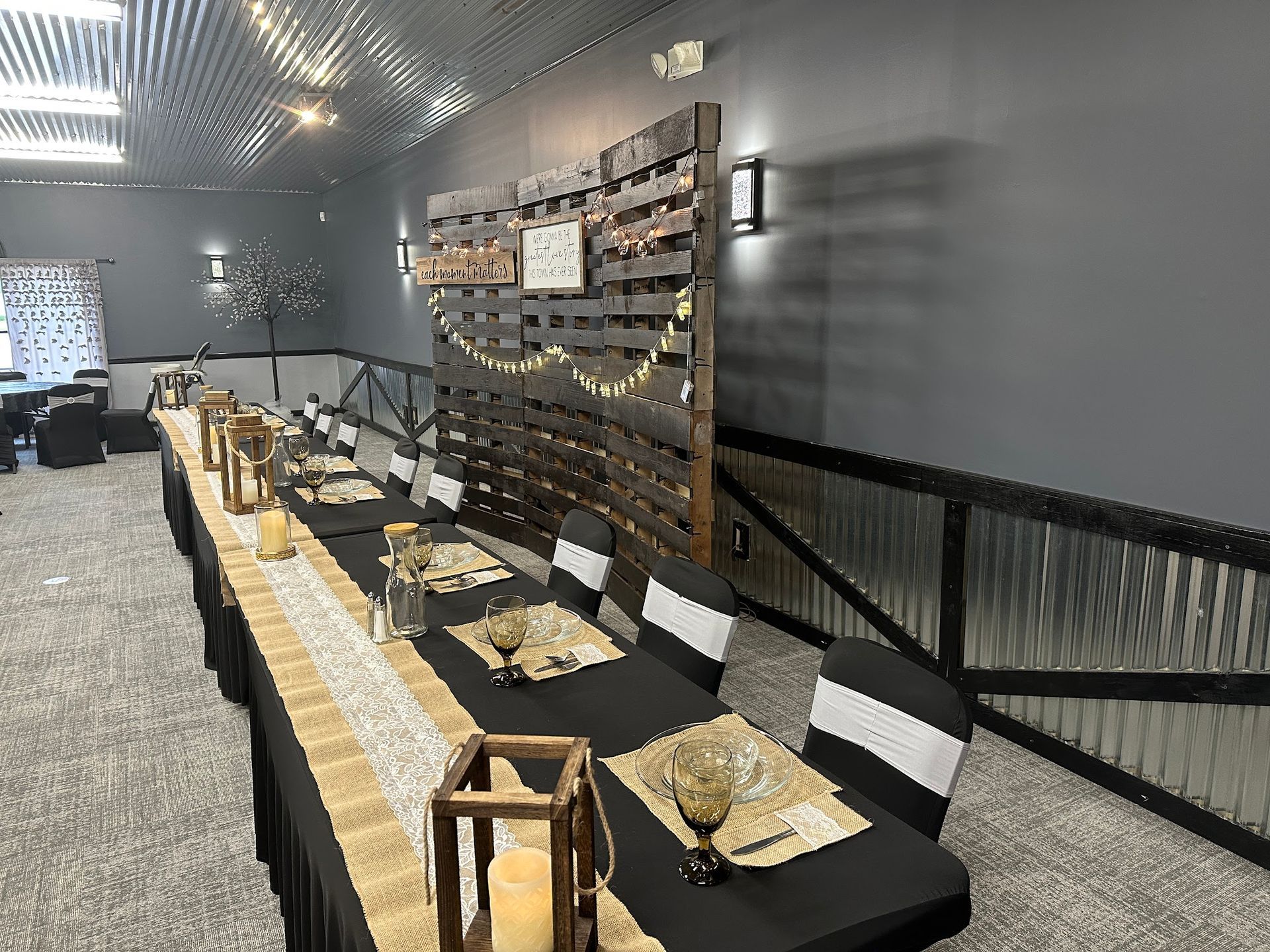 Modern indoor seating area with gray walls, black benches, a long wooden table, and lantern-style decor.