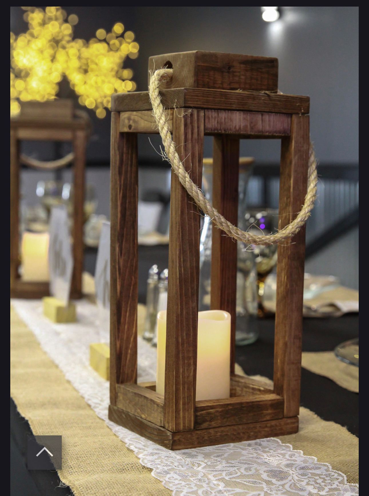 Rustic wooden lantern centerpiece with a candle and twine on a table runner