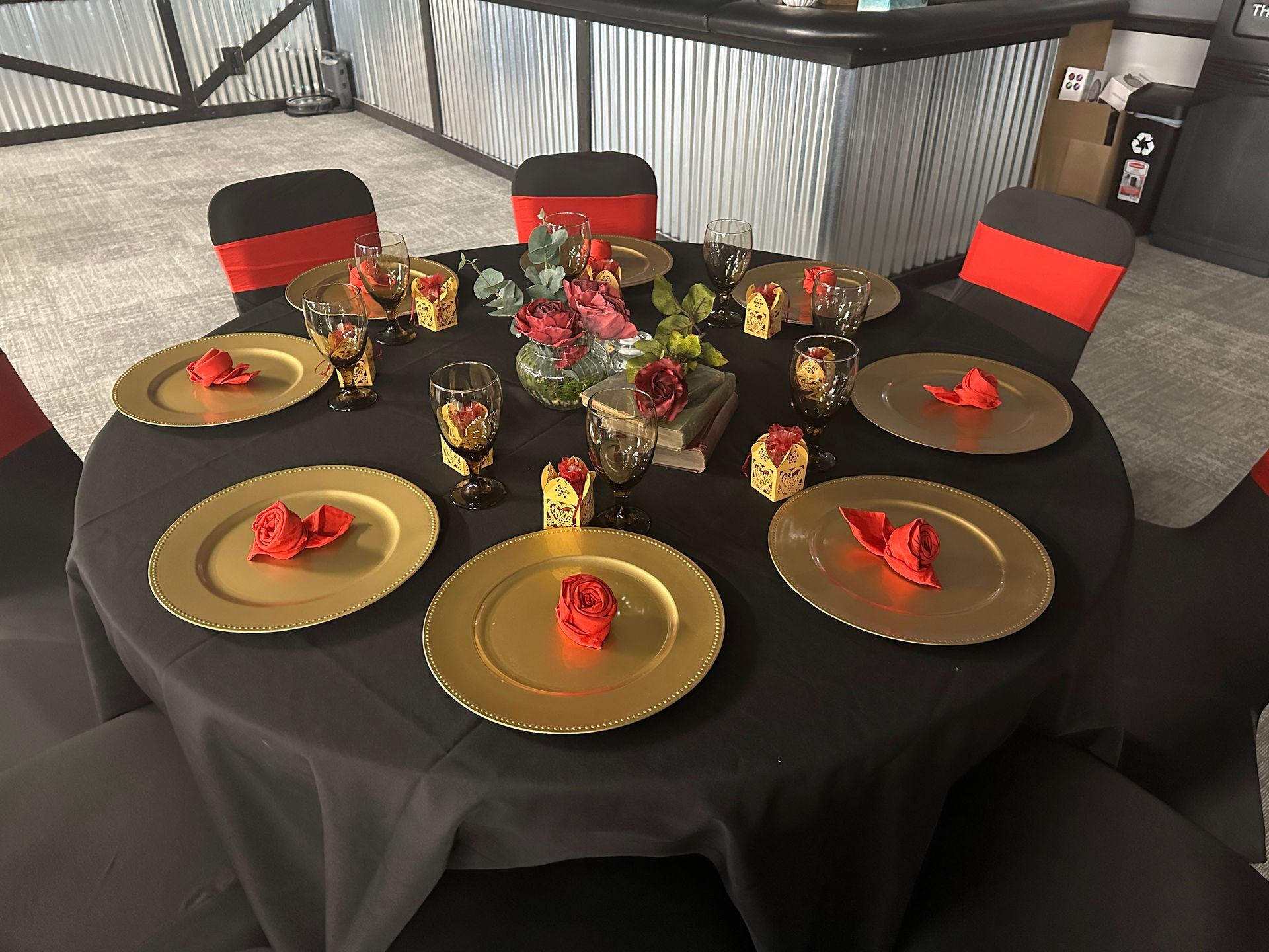 Round banquet table set with black linens, gold plates, red napkins, and floral centerpieces.