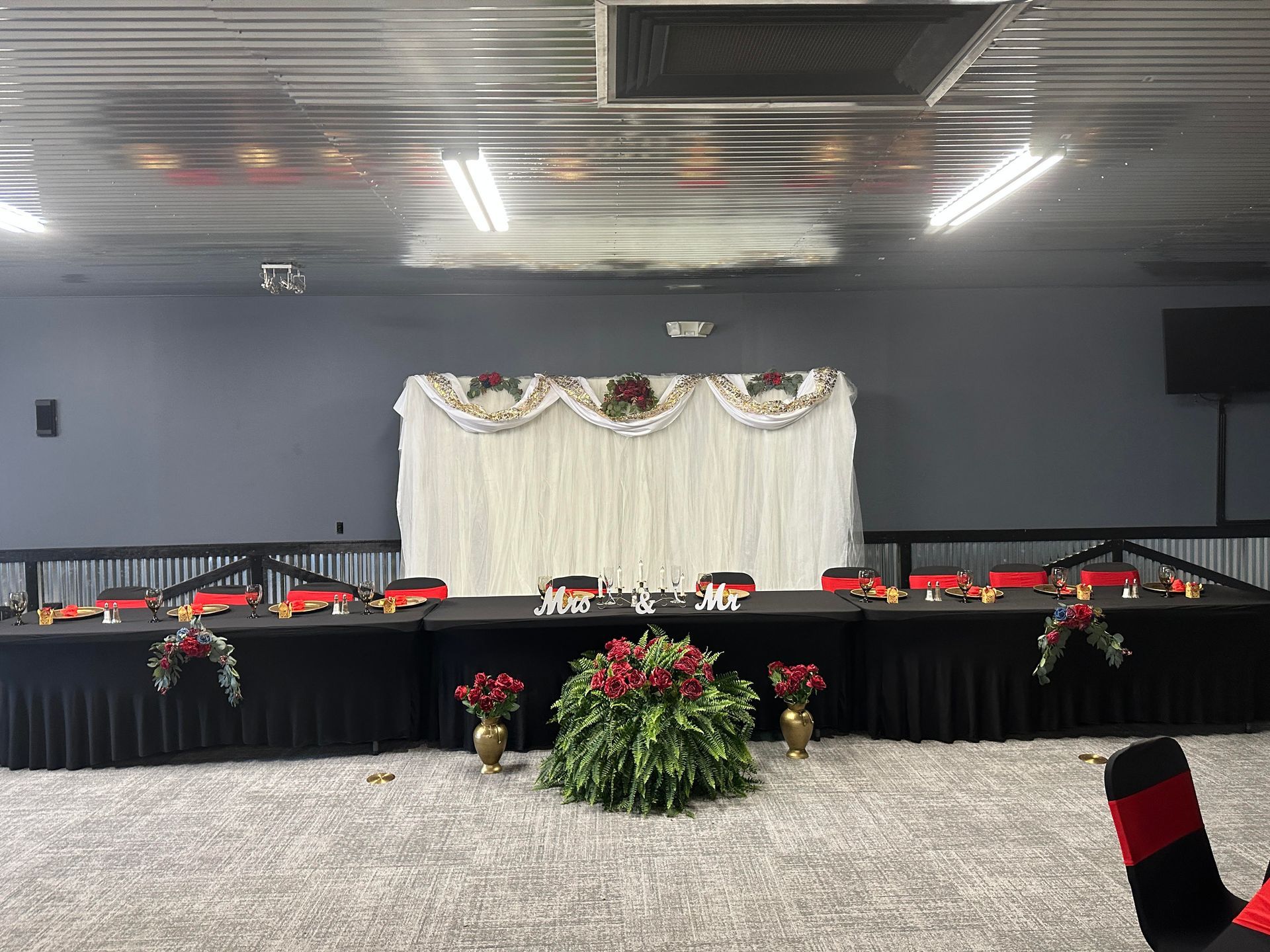 Decorated banquet stage with long black-draped tables, red floral arrangements, and a white backdrop