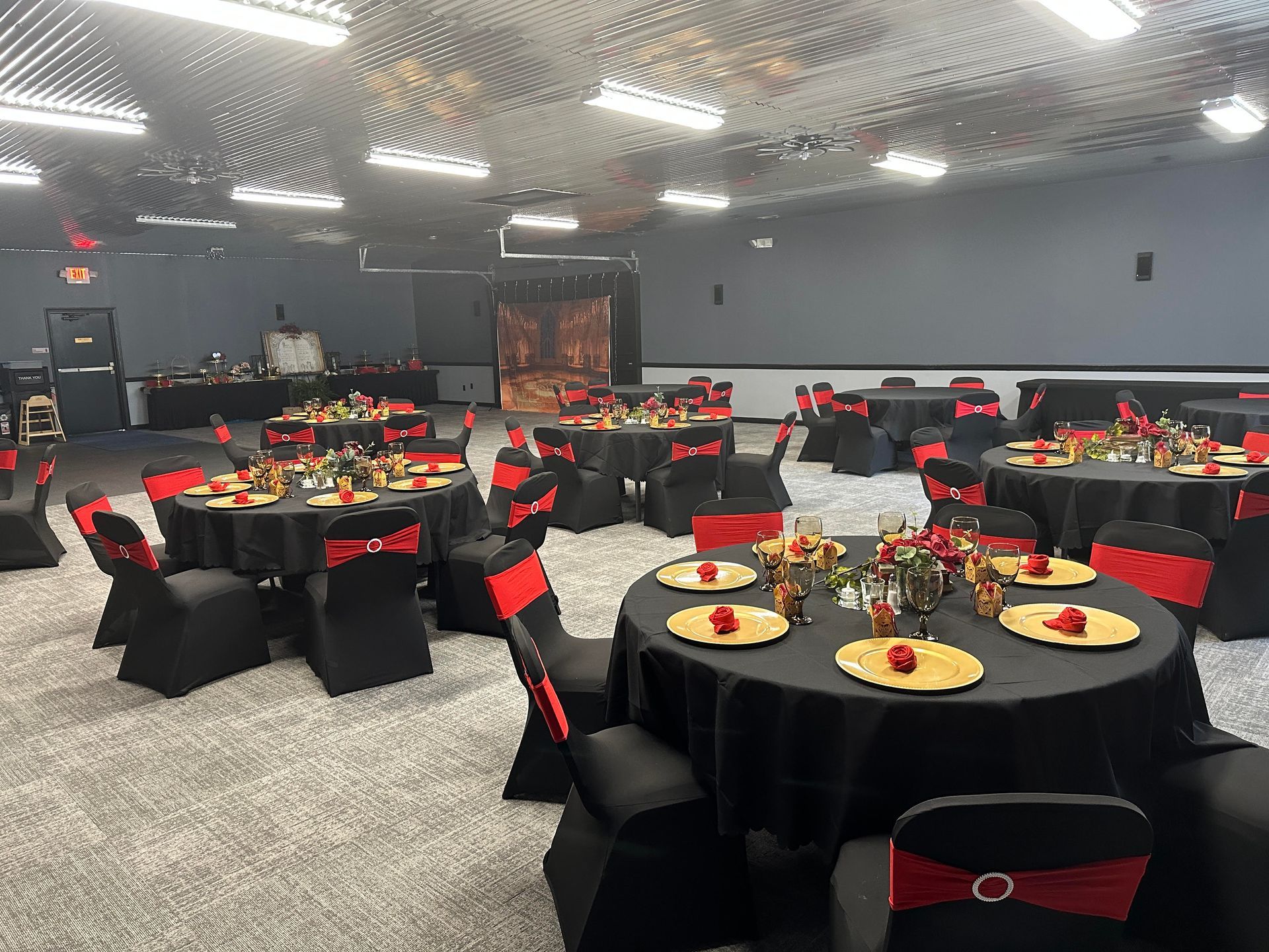 Banquet hall with round tables dressed in black and red chairs, set for an event under bright ceiling lights