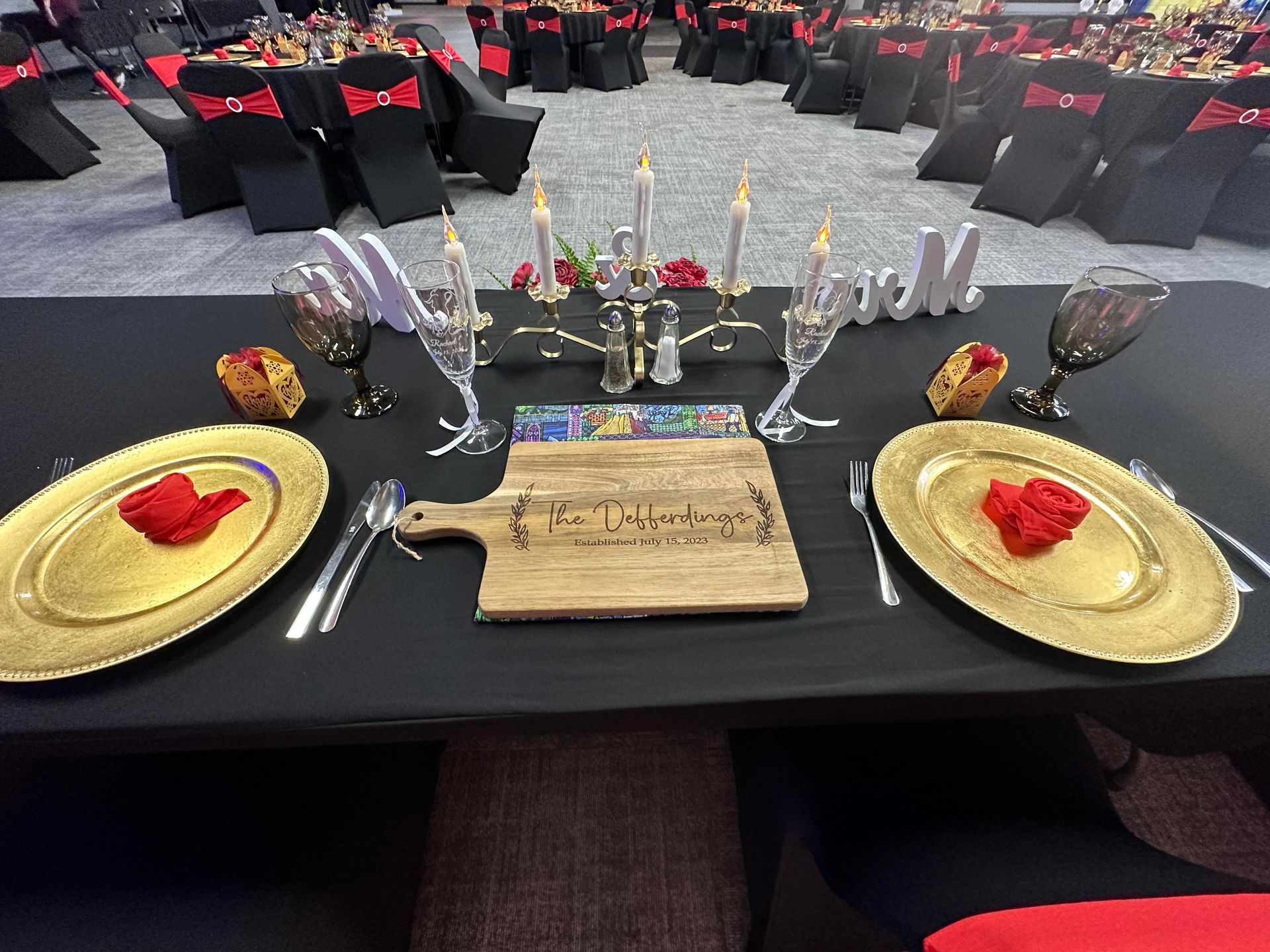 Table set with gold chargers, candles, and red roses in a black-and-red decorated banquet hall.