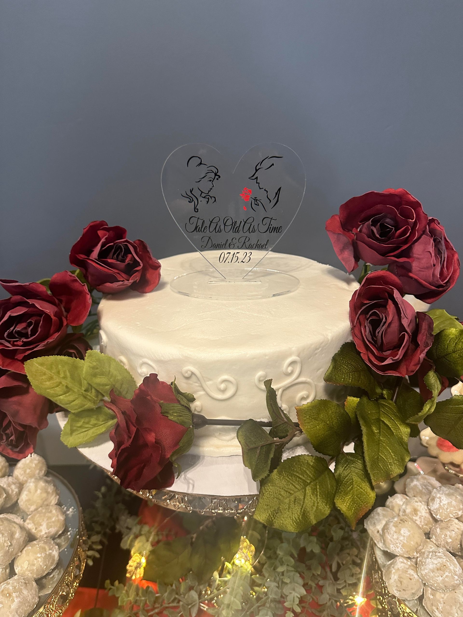 White frosted cake with red roses and heart topper on a sparkling table display