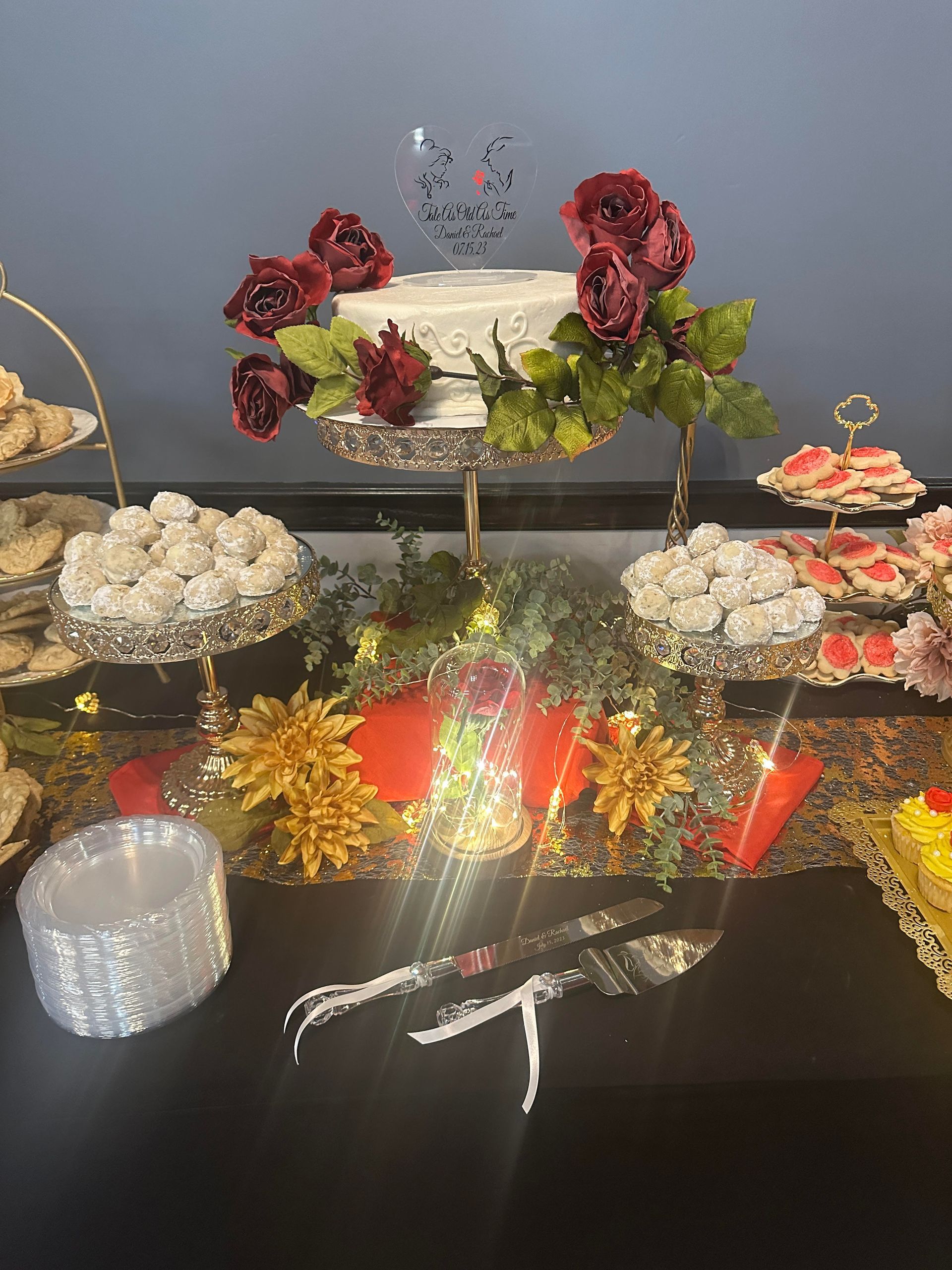 Decorative dessert display with layered cake, red and white floral arrangements, and gold accents on a black table