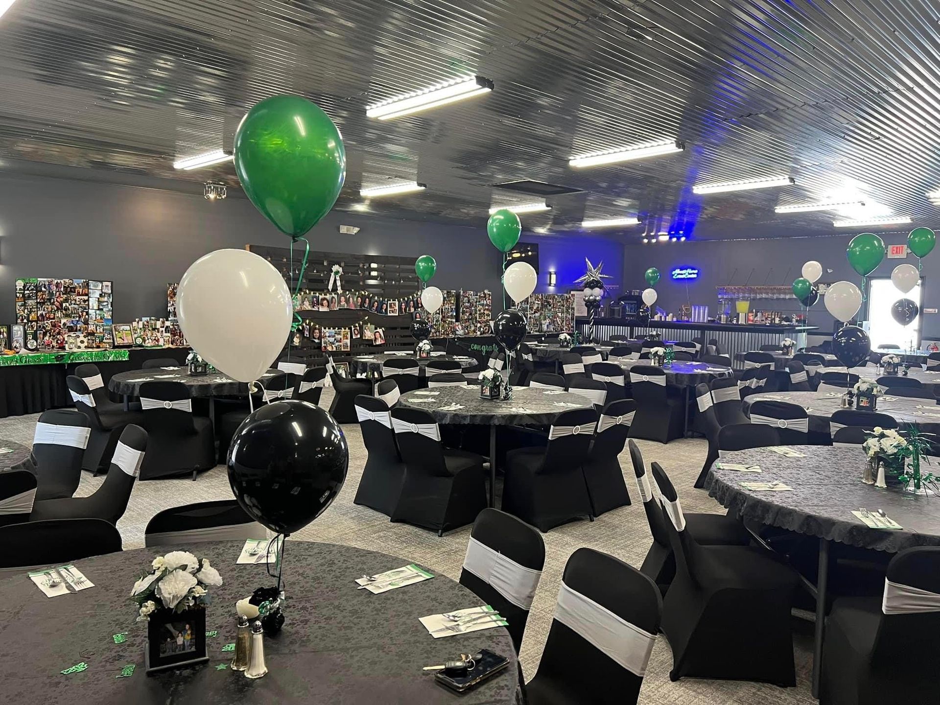 Decorated banquet hall with round tables, black-and-white chairs, and green, white, and black balloons