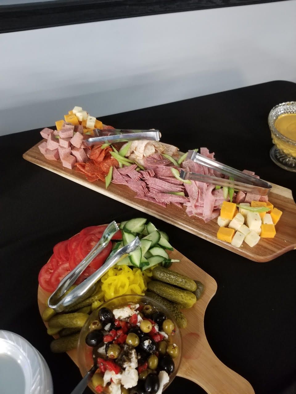 Assorted deli meats, cheese, olives, and pickles on wooden platters at a buffet spread