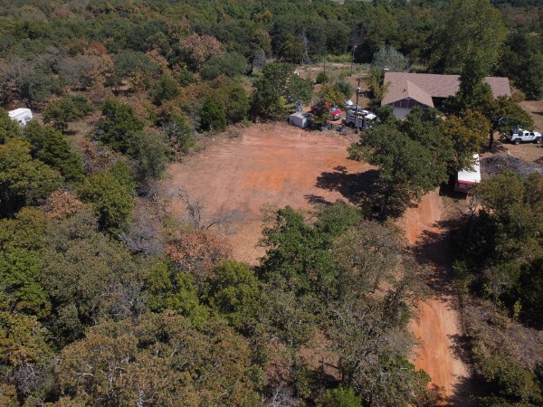 Aerial view of a dirt clearing in a wooded area beside a house and trees.