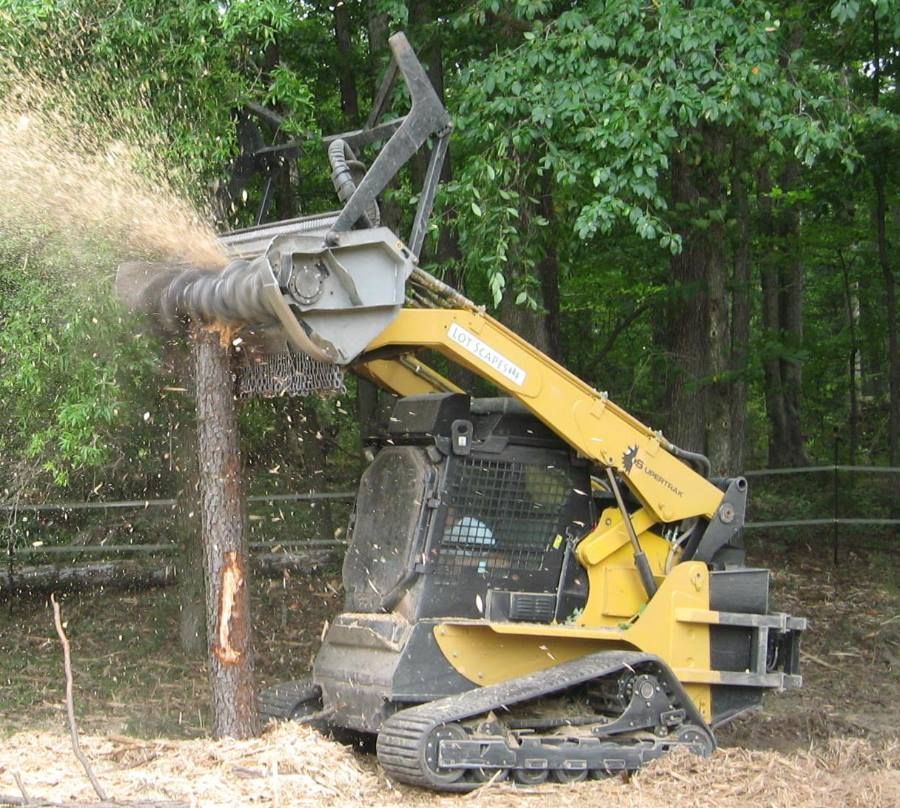 Yellow skid-steer with tree stump grinder attachment clearing a stump in a wooded area