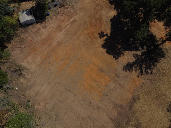 Aerial view of a dirt clearing with scattered trees and a small structure in the upper left corner.