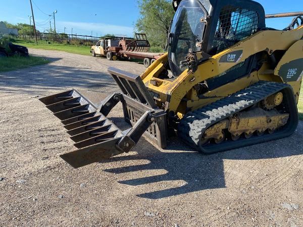 Yellow skid steer with bucket attachment on gravel lot, with trucks and equipment in the background