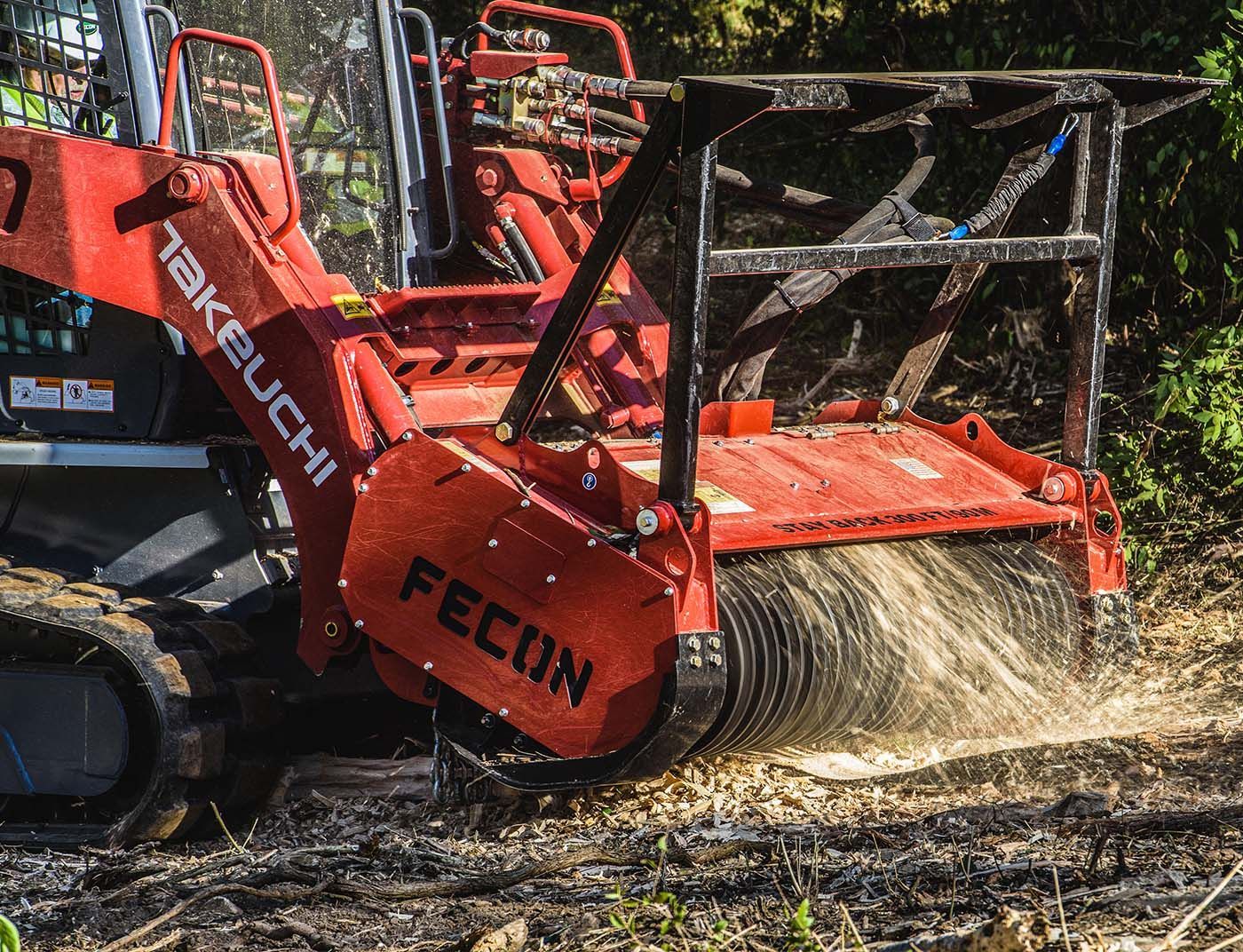 Red Fecon forestry mulcher grinding brush and ejecting debris in a wooded area