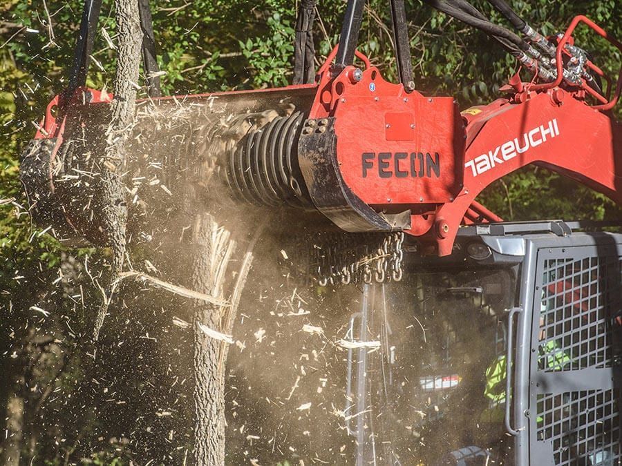 Red FECON forestry mulcher on a Yanmar excavator grinding vegetation, spraying debris.