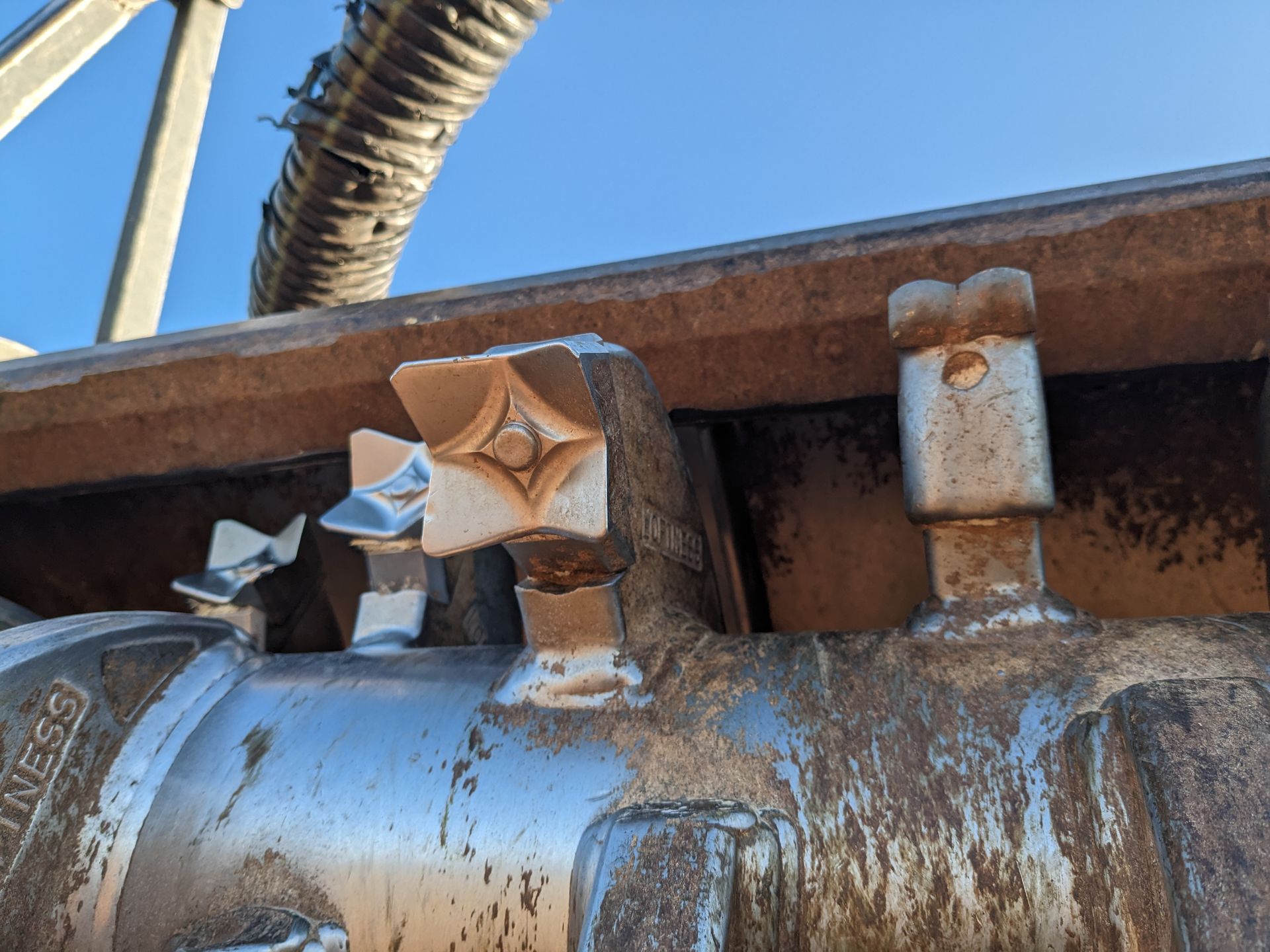 Rusty industrial pipe with star-shaped metal knobs under a blue sky