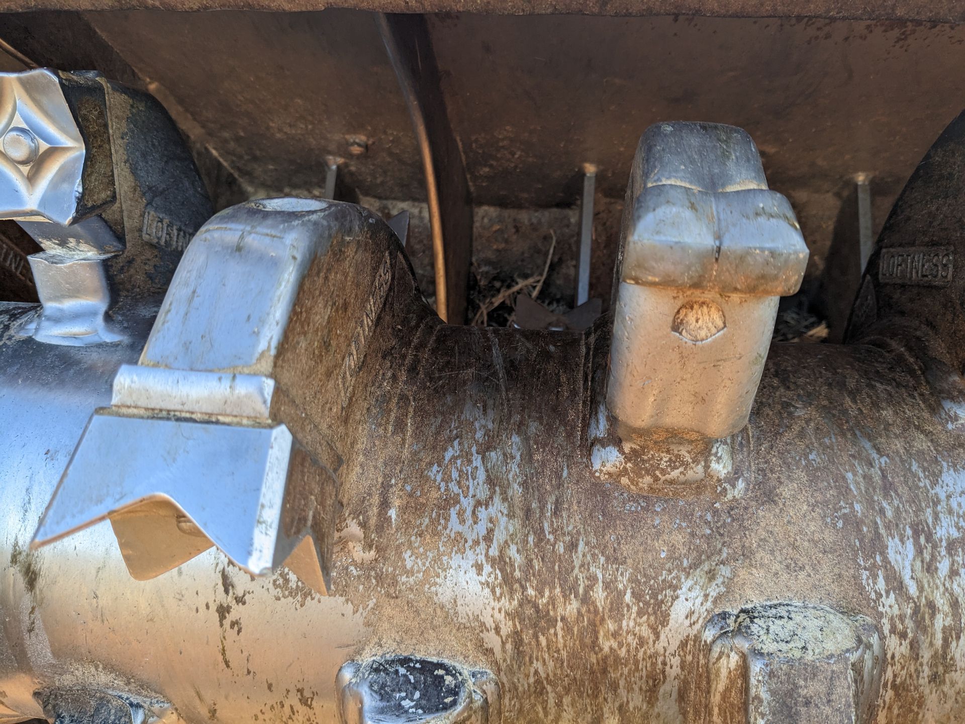 Close-up of dusty metal machinery parts with bolts and a hose in a dim industrial setting