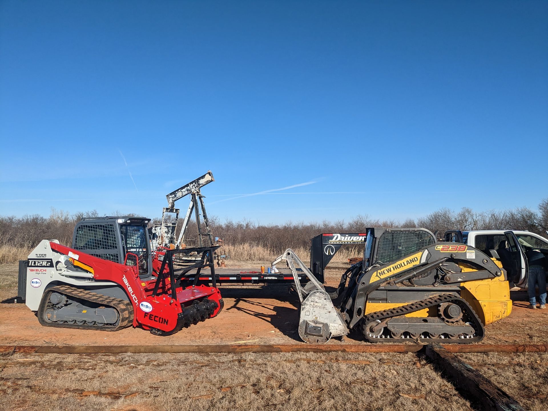 Two compact loaders facing each other on a dirt lot under a clear blue sky