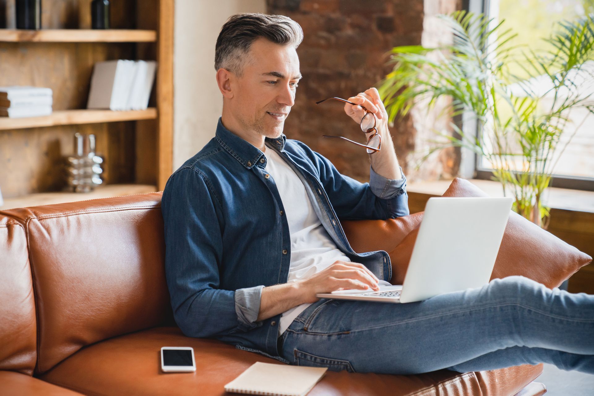 A man is sitting on a couch using a laptop computer.