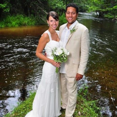 A bride and groom pose for a picture in front of a river