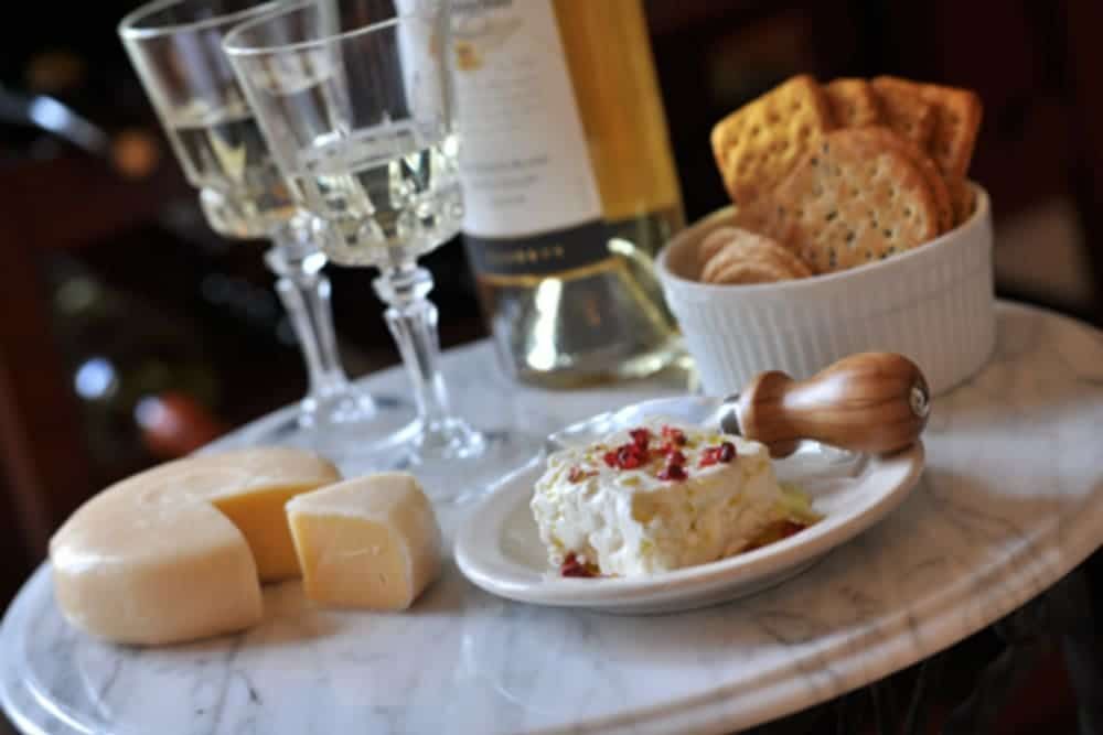 A table with a bottle of wine , crackers , cheese and wine glasses.