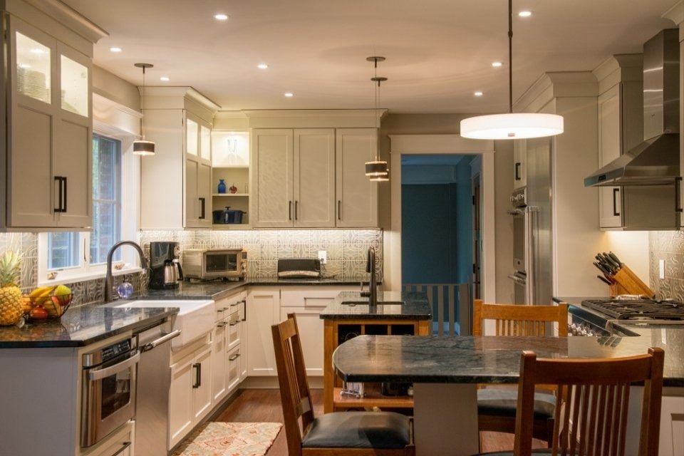 Modern kitchen with white cabinets, granite island, pendant lights, and a dining table by a blue doorway