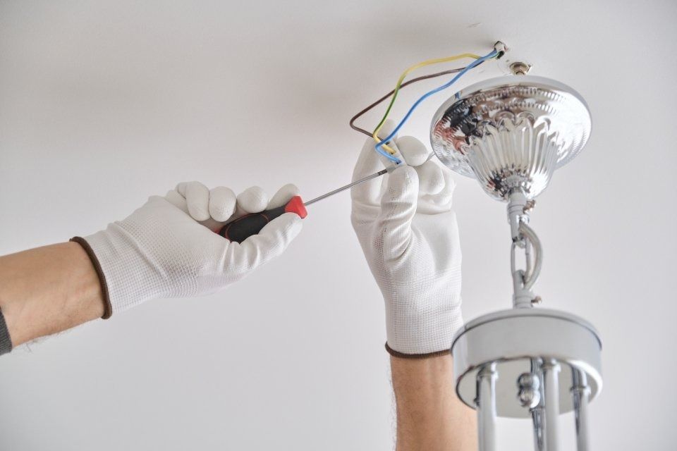 Gloved hands using a screwdriver to wire a ceiling light fixture