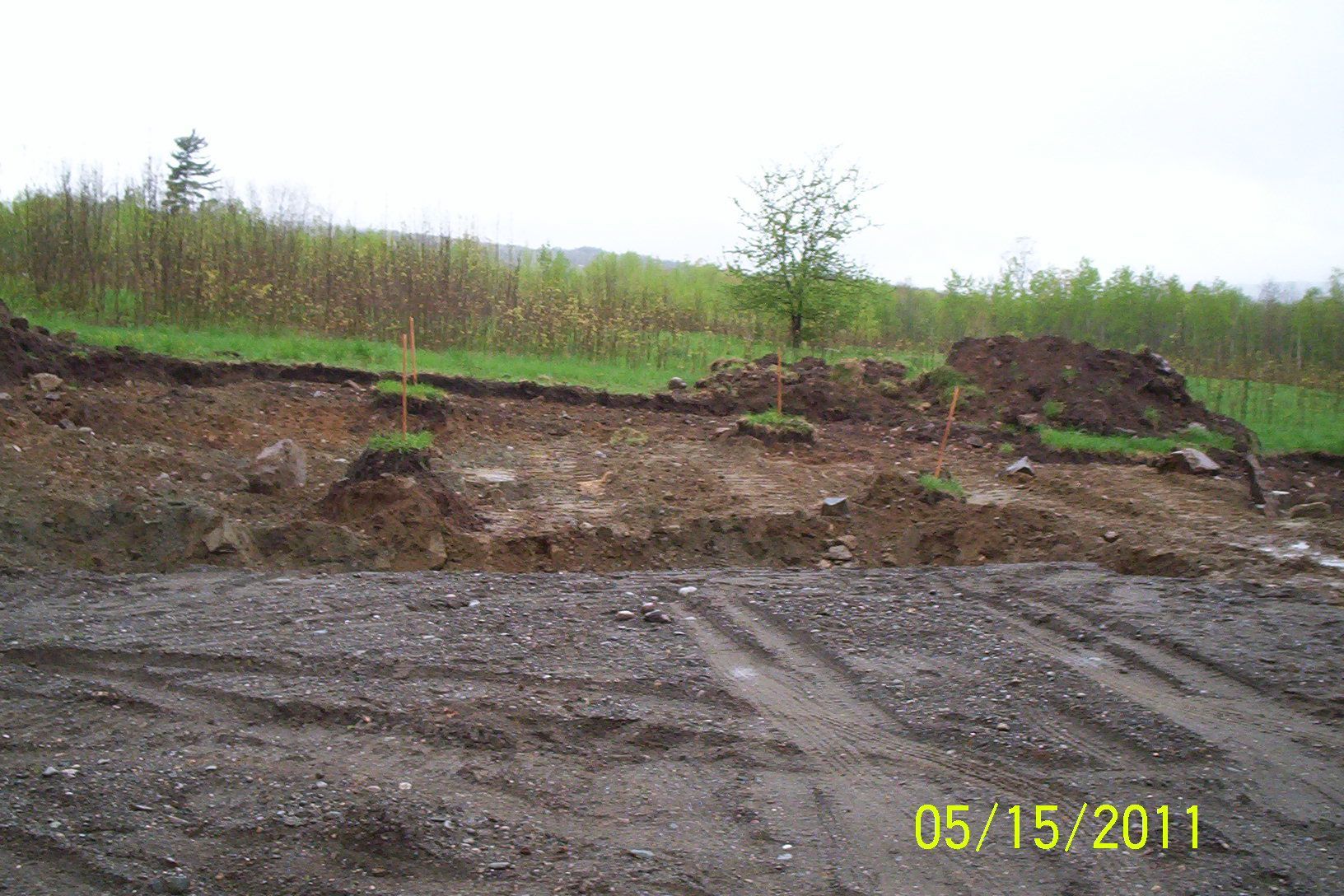 Eroded dirt slope above gravel lot with sparse green brush and a date stamp, 05/15/2011