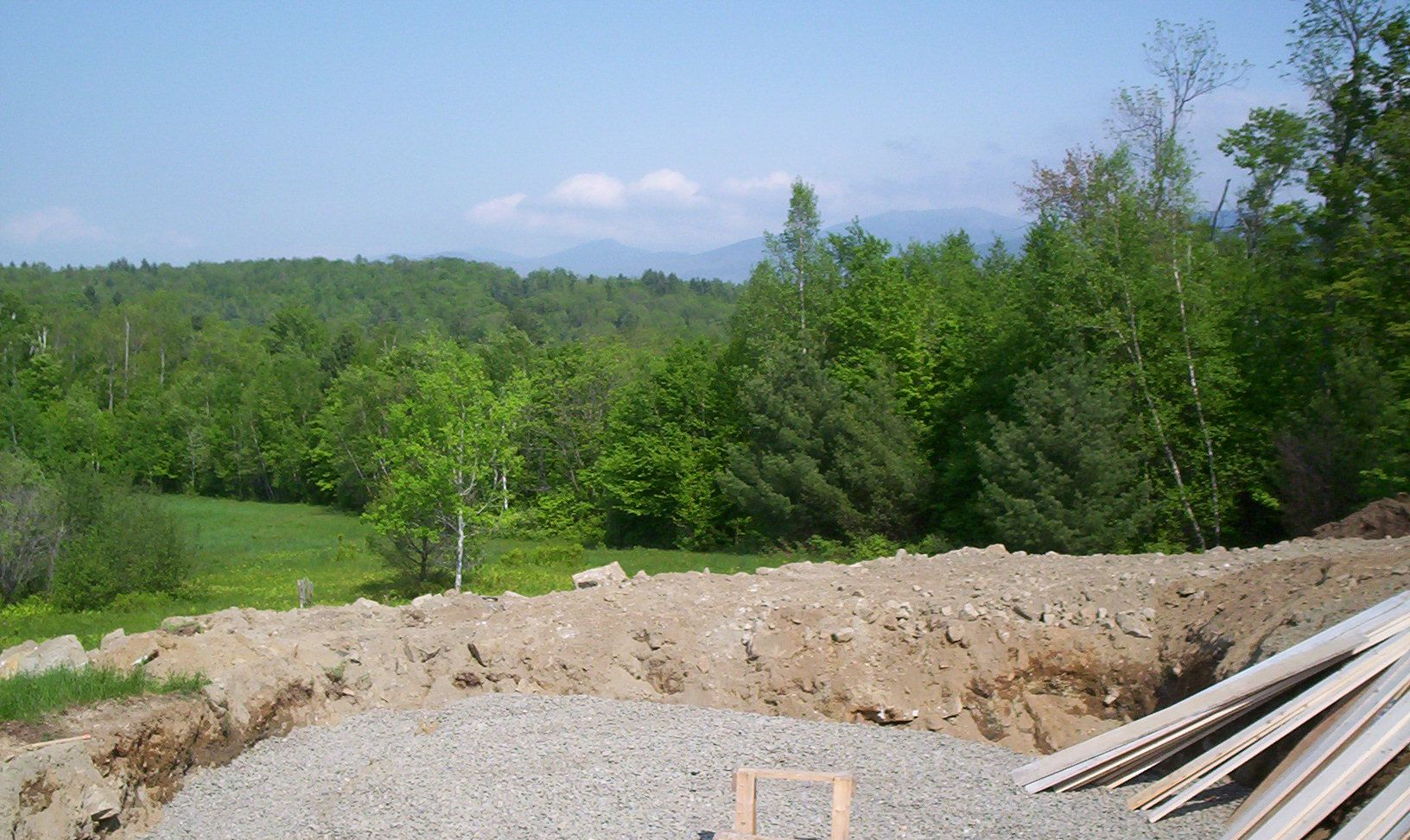 Gravel construction site overlooking green trees and hills under a clear blue sky