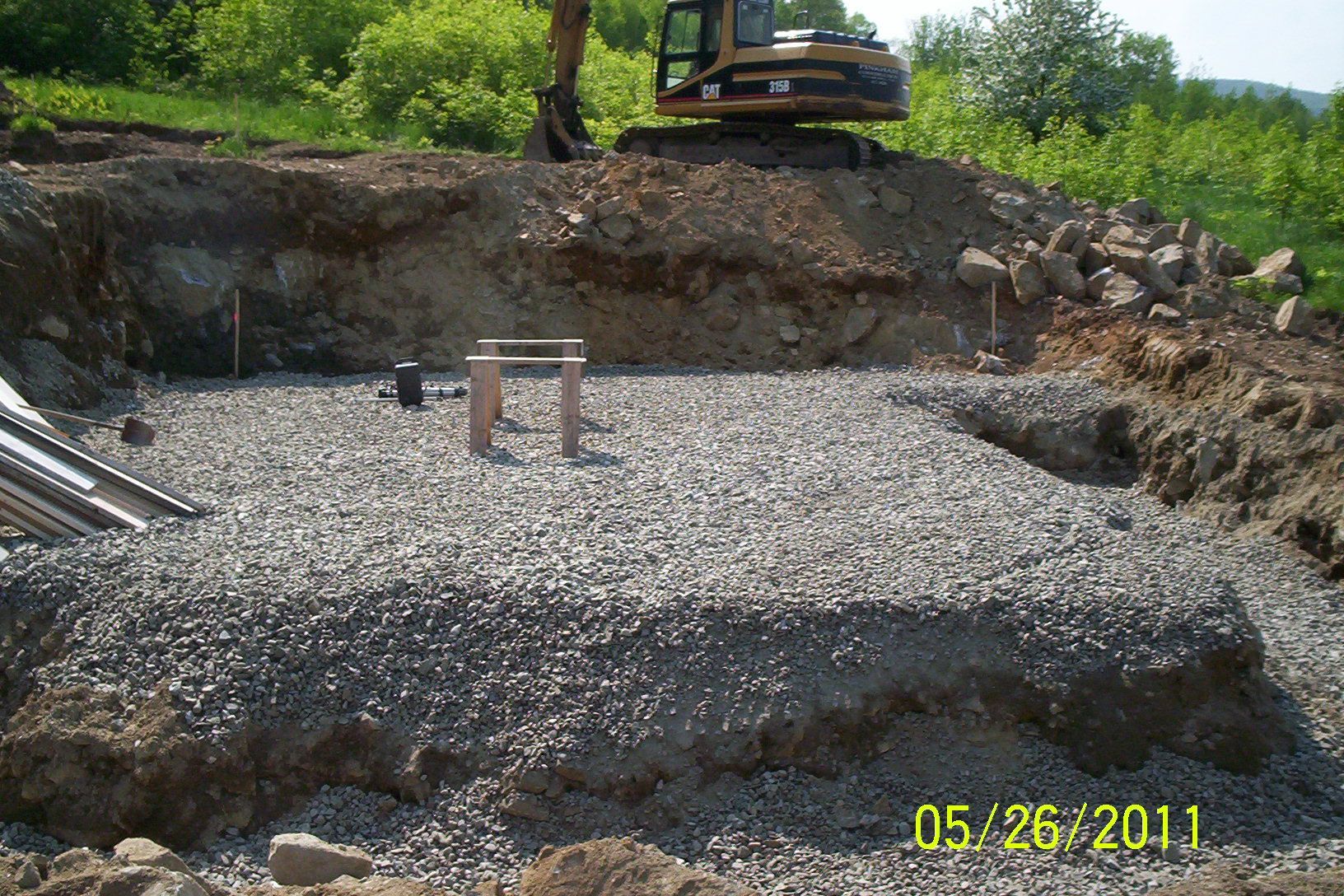 Excavated gravel foundation pit with a small table and yellow timestamp in the lower right.