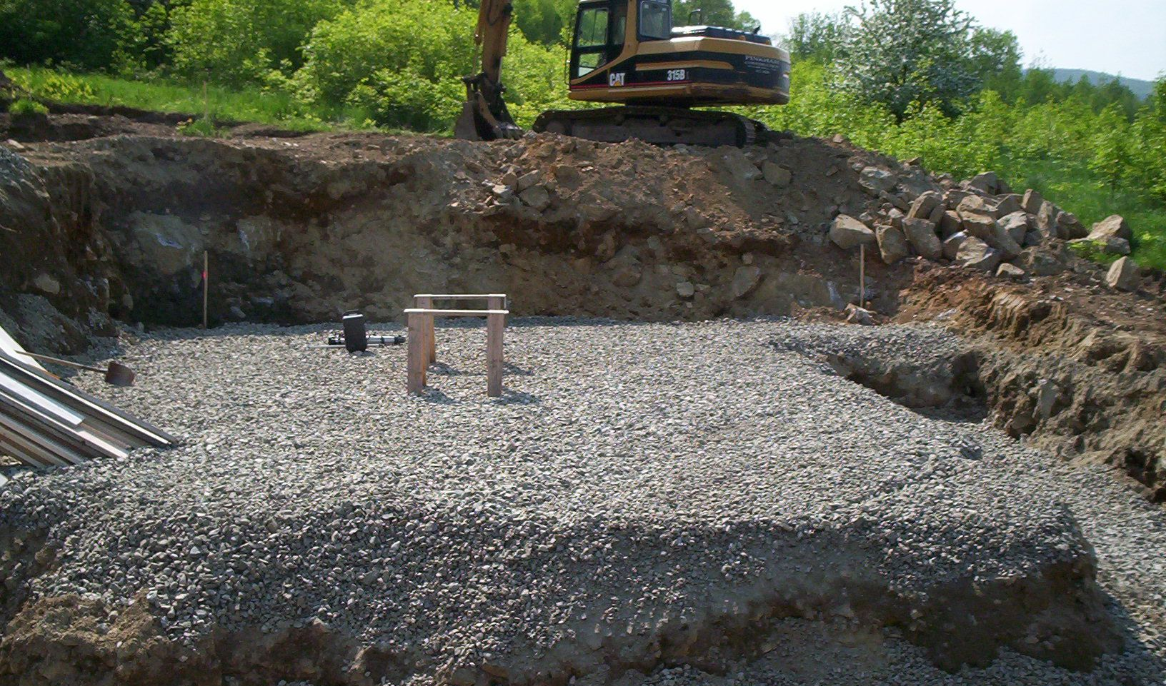 Excavation site with gravel base, dirt walls, and an excavator on the upper edge.