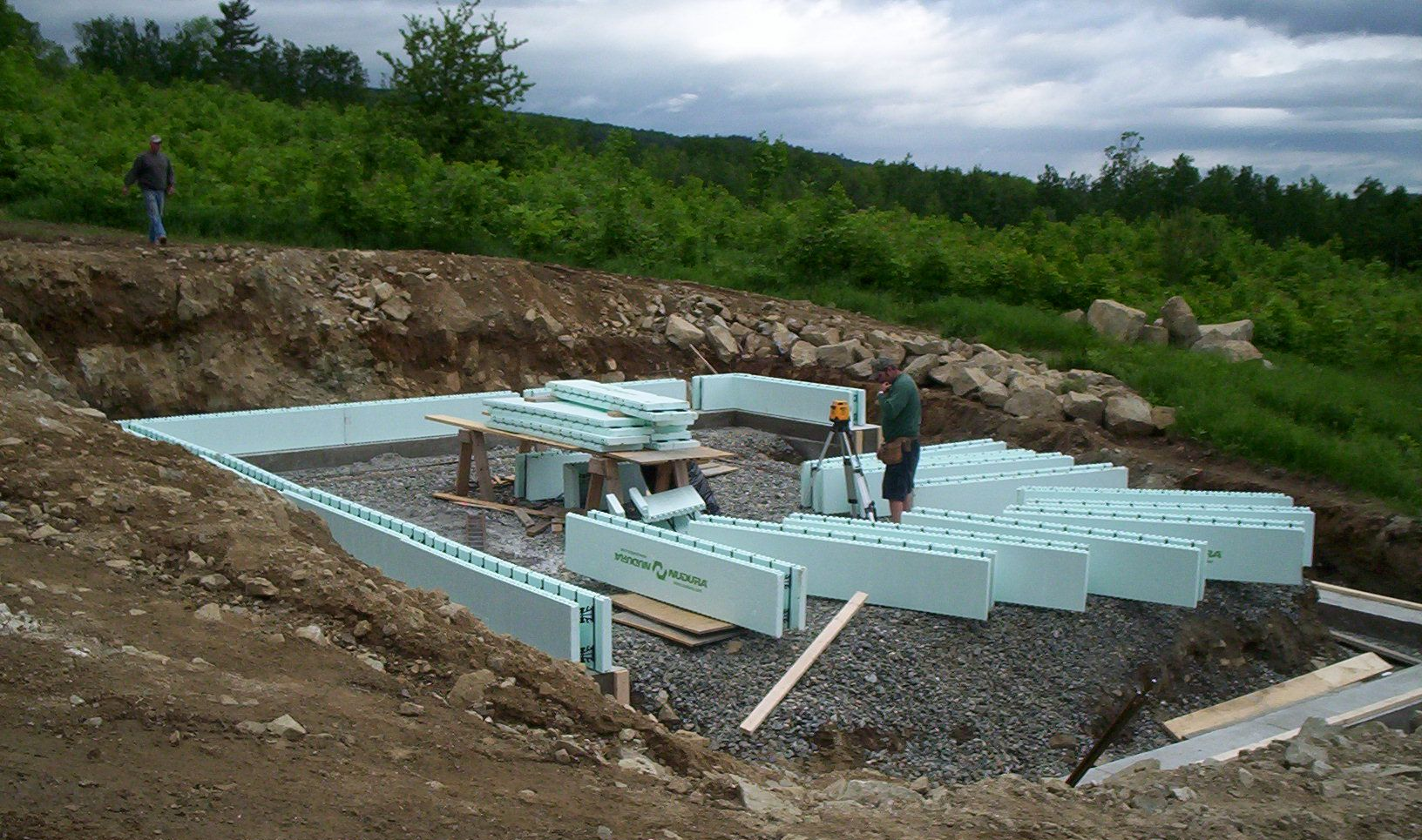 Workers installing light-blue insulated foundation walls at a house construction site.
