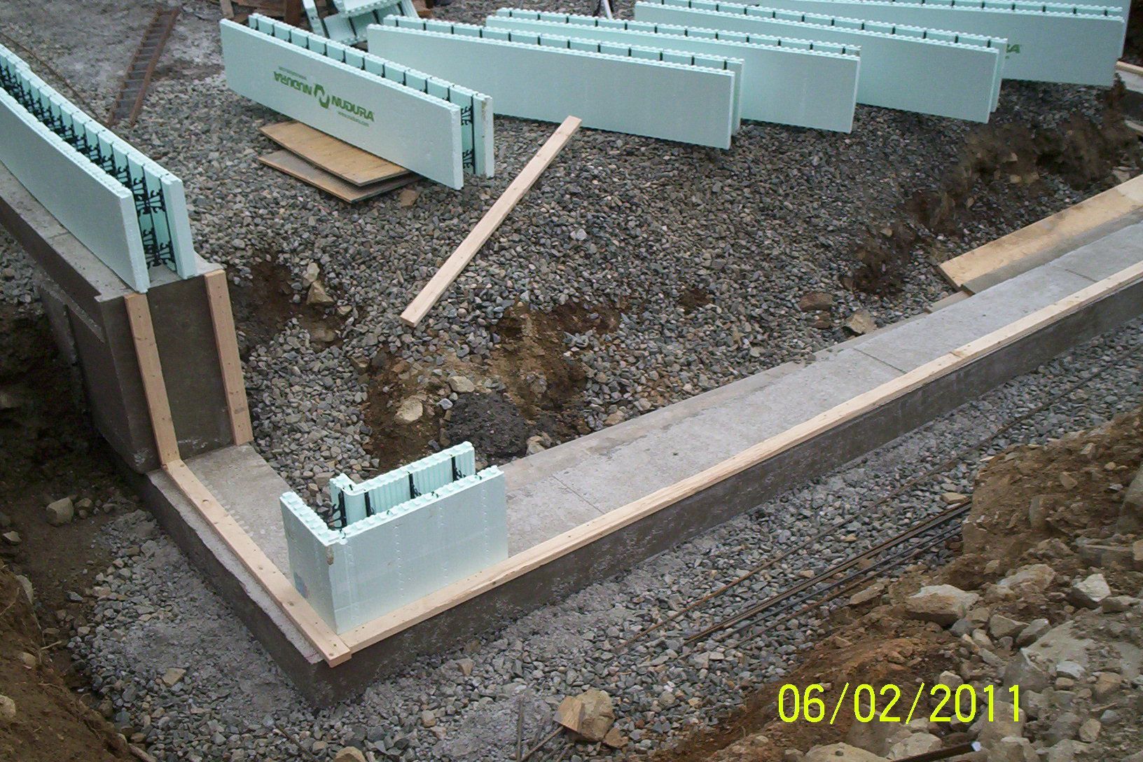 Partially built foundation with pale blue insulated wall forms and gravel footings at a construction site