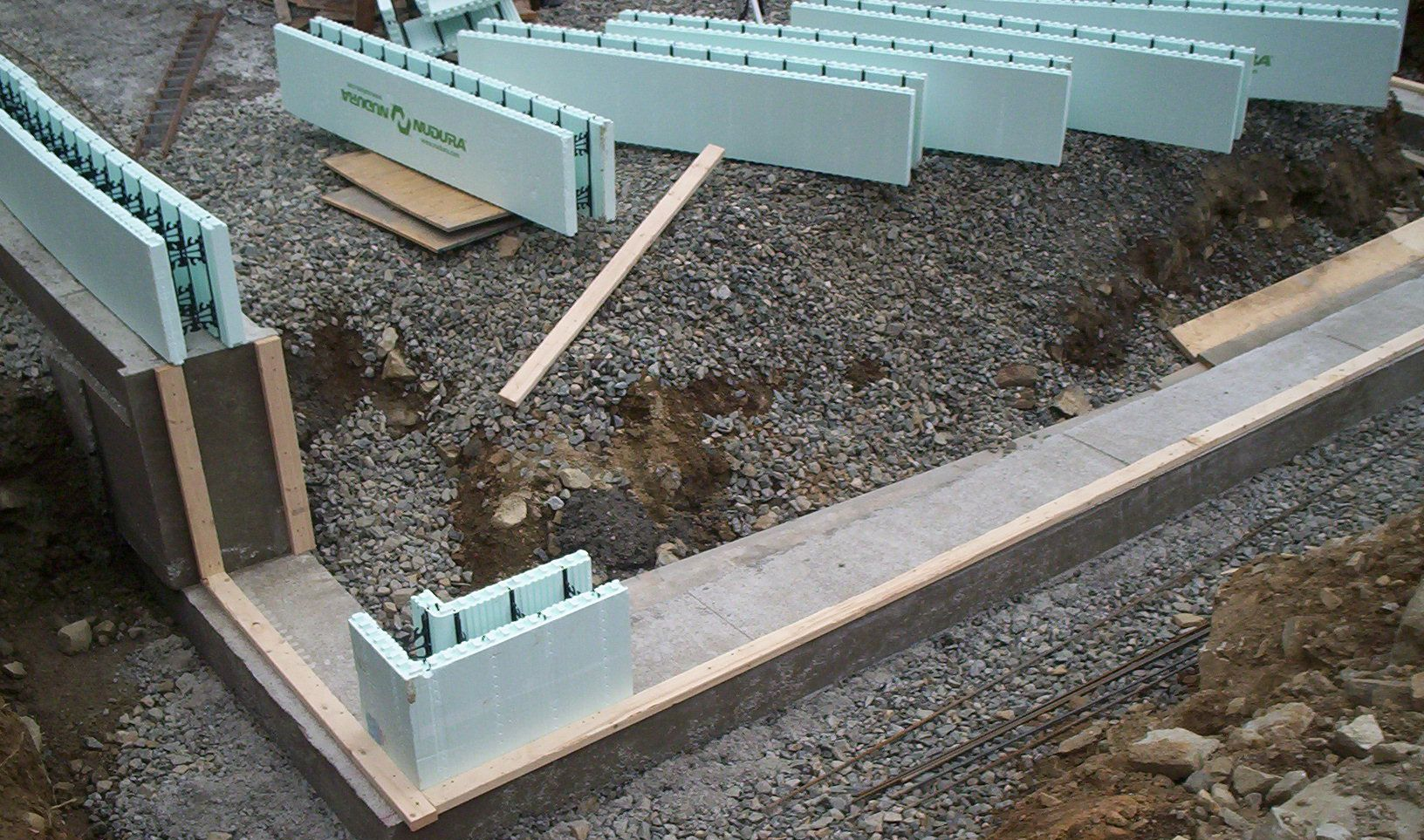 Foundation wall construction with green foam insulation panels and a gravel base in a trench